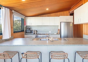 A modern kitchen with white cabinets, a stainless steel refrigerator, and a large window.