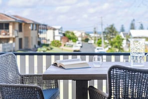 A balcony with wicker chairs, a table with a book and glasses, and a pitcher of water.