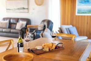 Una mesa de madera para comer con una botella de vino, copas y una tabla de quesos.