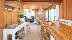 Een houten interieur met een eettafel, stoelen, een bank en een groot raam.