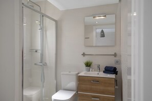 Ein modernes Badezimmer mit einer Glaskabine zur Dusche, einer Toilette, einem Waschbecken mit Spiegel darüber und Holzschränken.