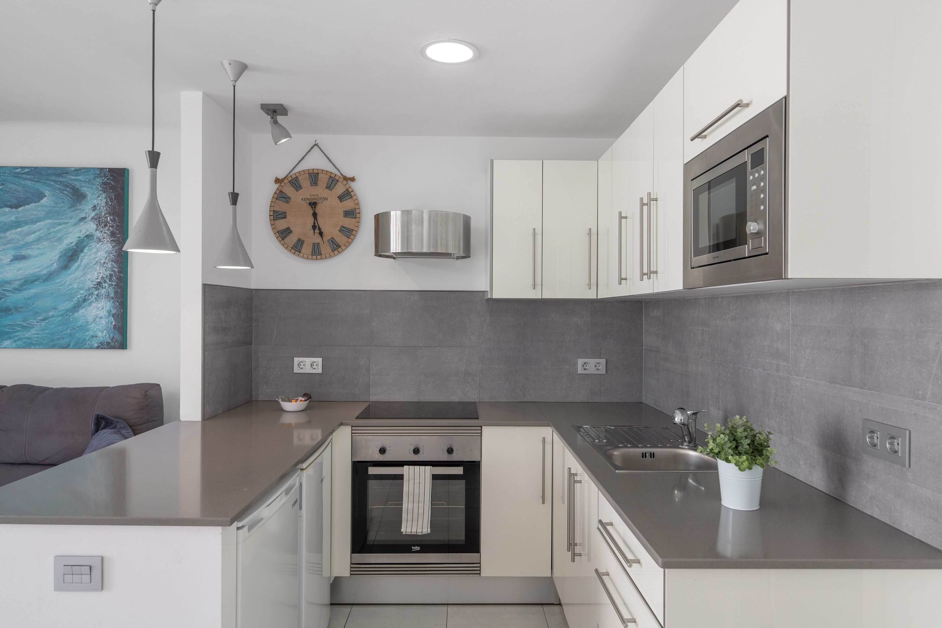 A modern kitchen with a built-in oven, stainless steel appliances, and a grey tiled backsplash.