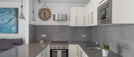 A modern kitchen with a built-in oven, stainless steel appliances, and a grey tiled backsplash.