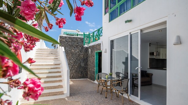 A building with a staircase leading to a balcony, a dining area with chairs and a table, and a green door. - Vacation 'Princesa Teguise' with Shared Pool, Shared Terrace and Wi-Fi (Tías)