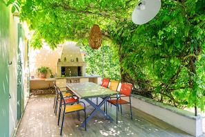 Un espace extérieur aménagé pour les repas, avec une table et des chaises, entouré de verdure et agrémenté d’une pergola.