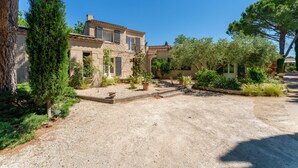 A courtyard with a gravel path, potted plants, and a stone building with windows. - Villa 'Charming with Pool' with Private Pool, Wi-Fi and Air Conditioning (Fontvieille)