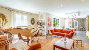 A living room with a piano, orange sofa, and a dining area with a table and chairs. - Villa 'Charming with Pool' with Private Pool, Wi-Fi and Air Conditioning (Fontvieille)