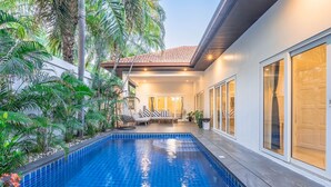Una casa moderna con piscina, rodeada de exuberante vegetación y un patio con mobiliario de exterior.