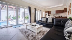 Amplia sala de estar con un sofá negro, una mesa de centro blanca y un ventanal de vidrio que da a un balcón con piscina.