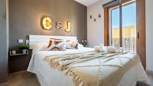 Un dormitorio con una cama, una mesita de noche, una lámpara de pared y una ventana con vistas.