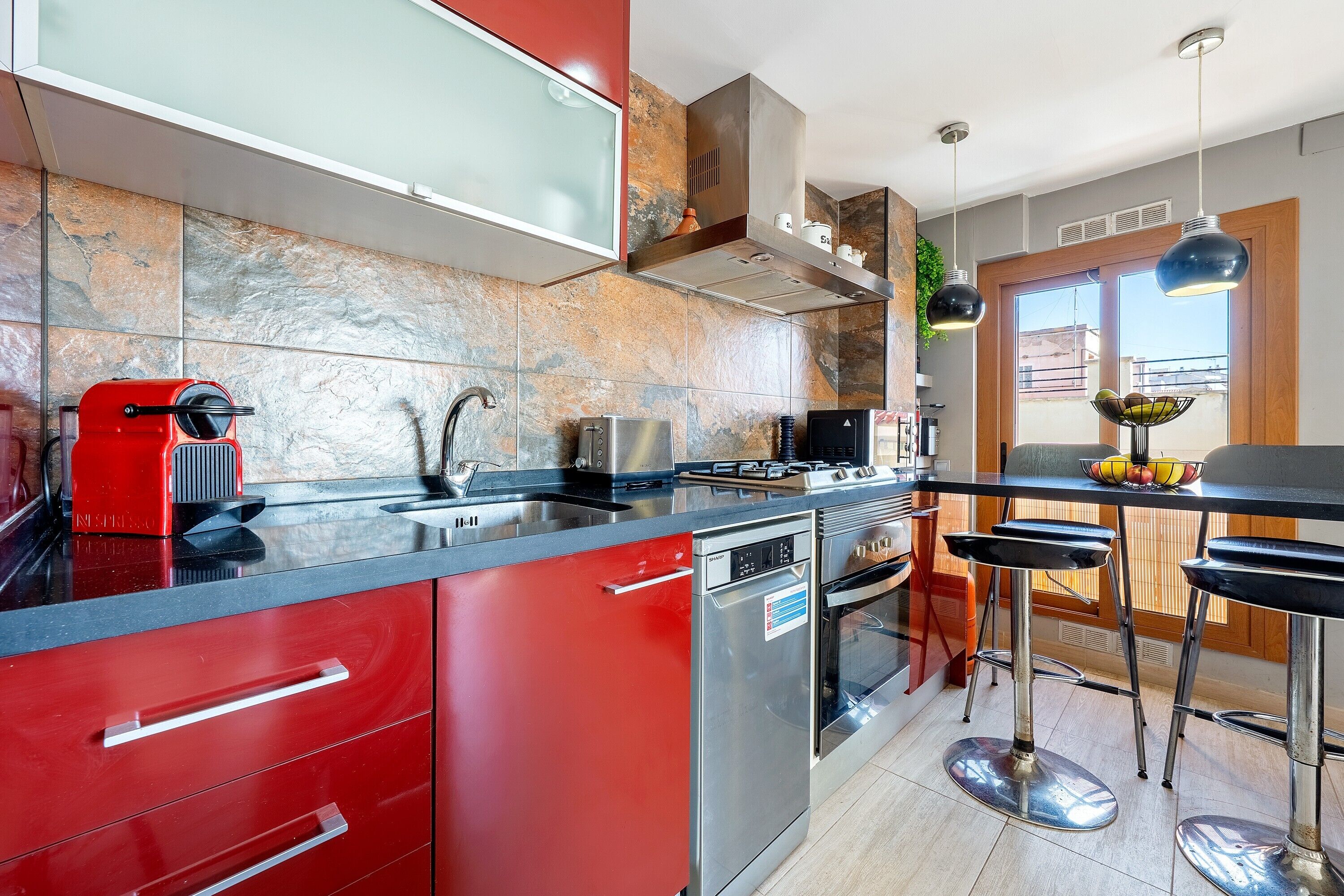 A modern kitchen with red cabinetry, stainless steel appliances, and a bar area with stools.