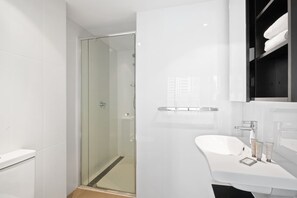 Ein modernes Badezimmer mit Duschkabine aus Glas, einem weißen Waschbecken mit Spiegel und einem Handtuchhalter.