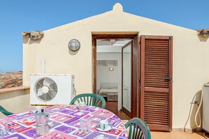 Un patio con una mesa lista para dos personas, un equipo de aire acondicionado y una puerta que da a un dormitorio.