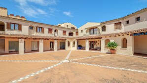A courtyard with a tiled floor, buildings with arched doorways, and a sign reading 'SCUOLA G.' - Apartment 'Piazzetta Garden' with Sea View, Private Terrace and Air Conditioning (san teodoro)
