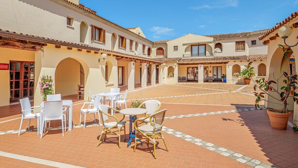 An outdoor patio area with white chairs and tables, surrounded by buildings with arches and a tiled roof. - Apartment 'Piazzetta Garden' with Sea View, Private Terrace and Air Conditioning (san teodoro)