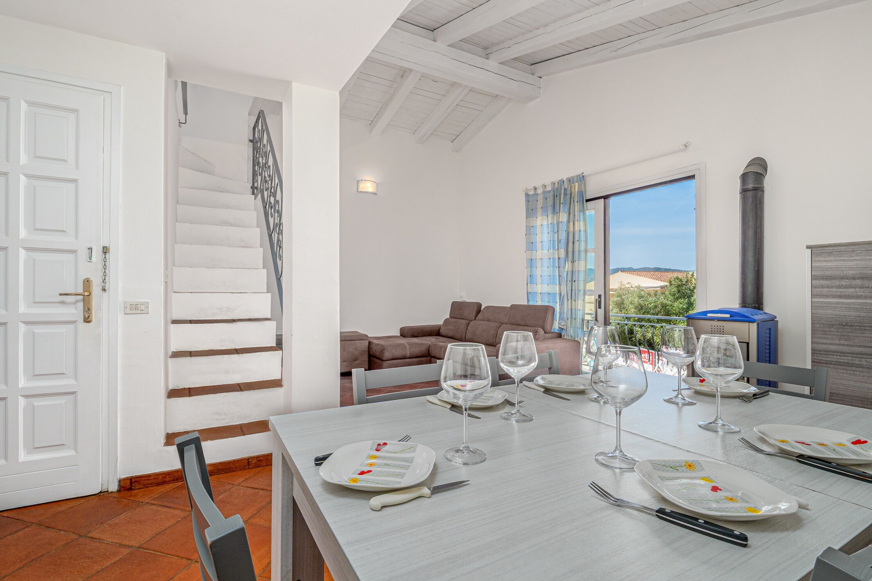 A dining area with a table set for four, a staircase, a sofa, and a view of the outdoors.