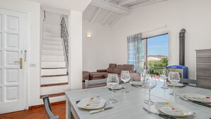 A dining area with a table set for four, a staircase, a sofa, and a view of the outdoors. - Apartment 'Piazzetta Garden' with Sea View, Private Terrace and Air Conditioning (san teodoro)