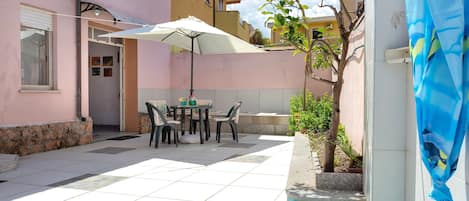 Eine Terrasse mit Tisch und Stühlen, ein Pool und ein Gebäude mit rosafarbenem Mauerwerk.