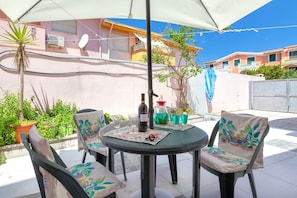 Um pátio com uma mesa, cadeiras, uma garrafa de vinho e um jarro.