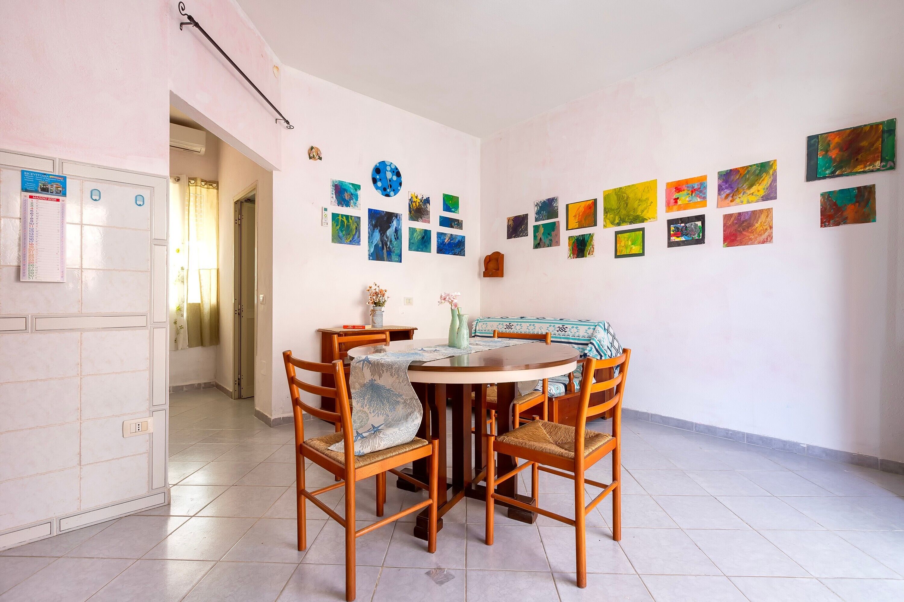 Un comedor con una mesa redonda, cuatro sillas y una pared decorada con varias obras de arte.