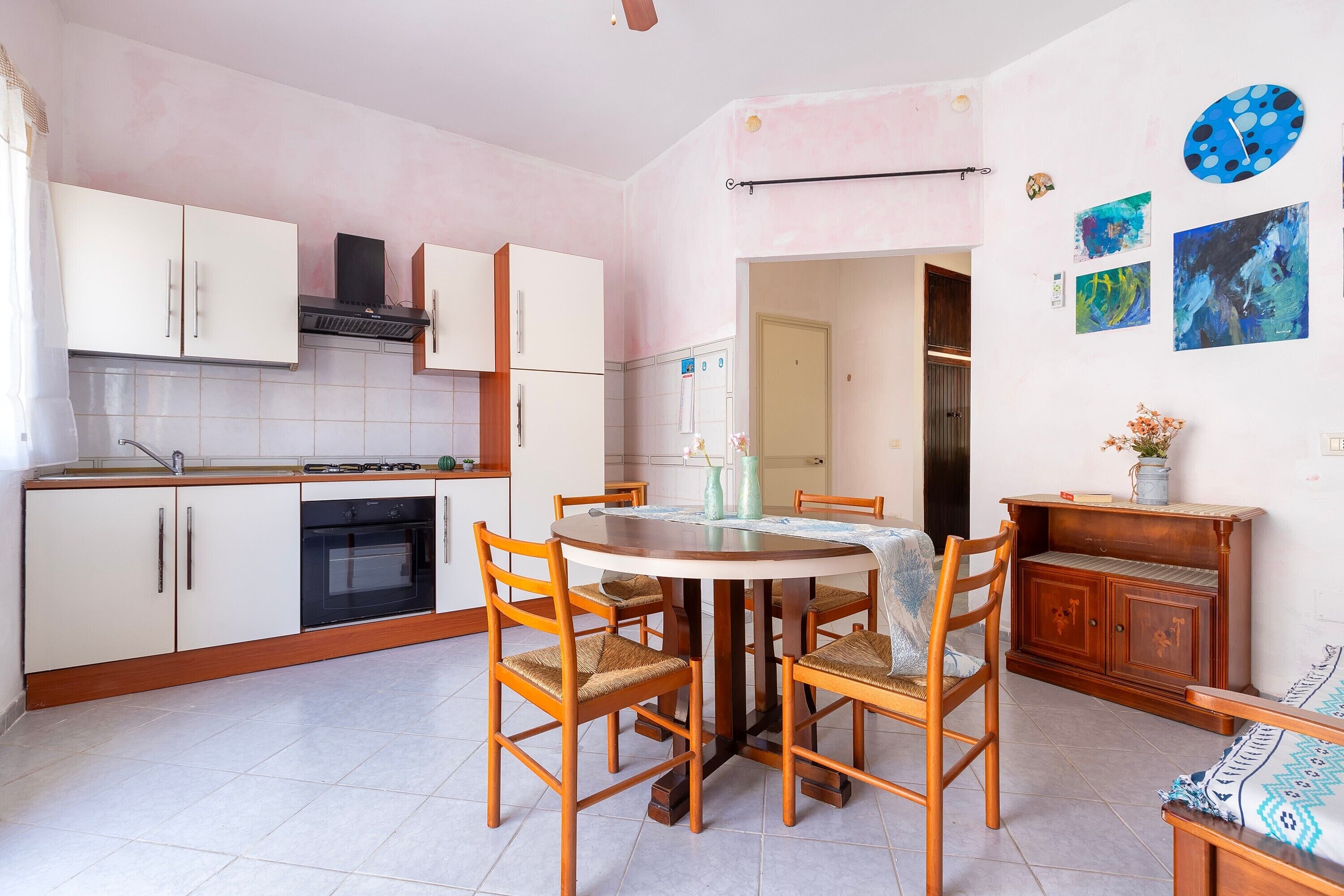 Una cocina con armarios blancos, una mesa de comedor con sillas y un mueble de madera con una planta.