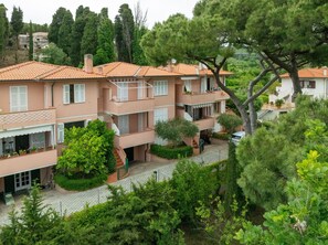Un edificio residencial de varios pisos con balcones, un camino pavimentado y follaje circundante.