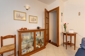 A room with a wooden cabinet, a chair, a small table with a vase, and a door leading to another room.