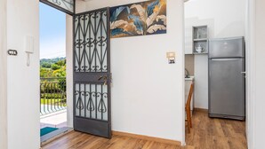 Een kamer met een houten vloer, een grijze koelkast, een decoratief wandobject en een deur met een metalen hekwerk.
