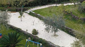 Een tuin met een schommel, grindpaden en verschillende planten.