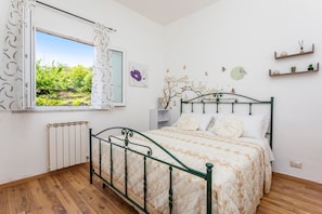 A bedroom with a bed, a window with curtains, a radiator, and wall decorations. - Apartment 'Sara' with pool, sea & Etna view, private terrace (Mascali)
