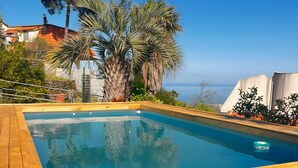 Een houten terras met een zwembad, palmbomen en uitzicht op zee.