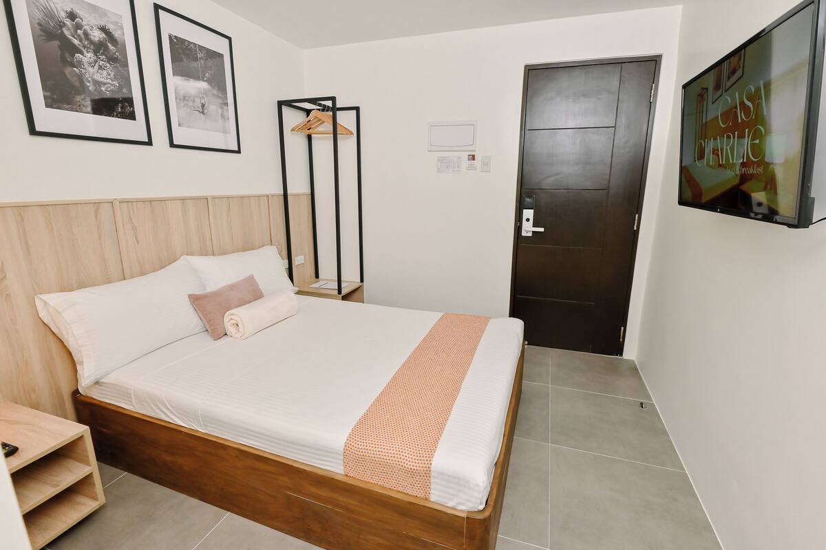 A neatly made bed with a wooden headboard, a single hanging coat rack, and a framed picture on the wall.
