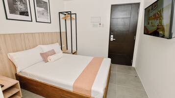 A neatly made bed with a wooden headboard, a single hanging coat rack, and a framed picture on the wall.