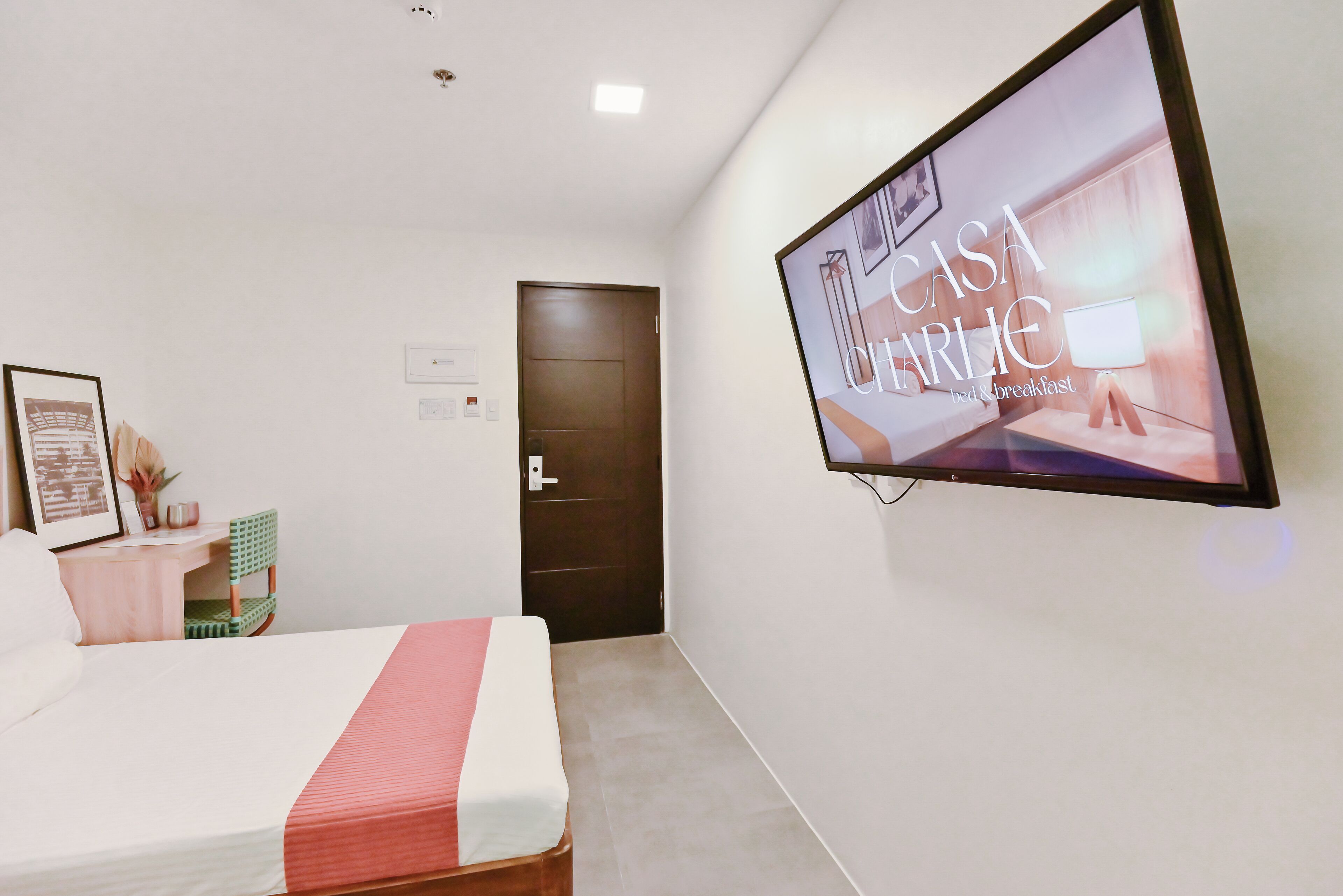 Una camera d'albergo con un letto, una televisione a muro, una porta e un piccolo tavolo con una sedia.