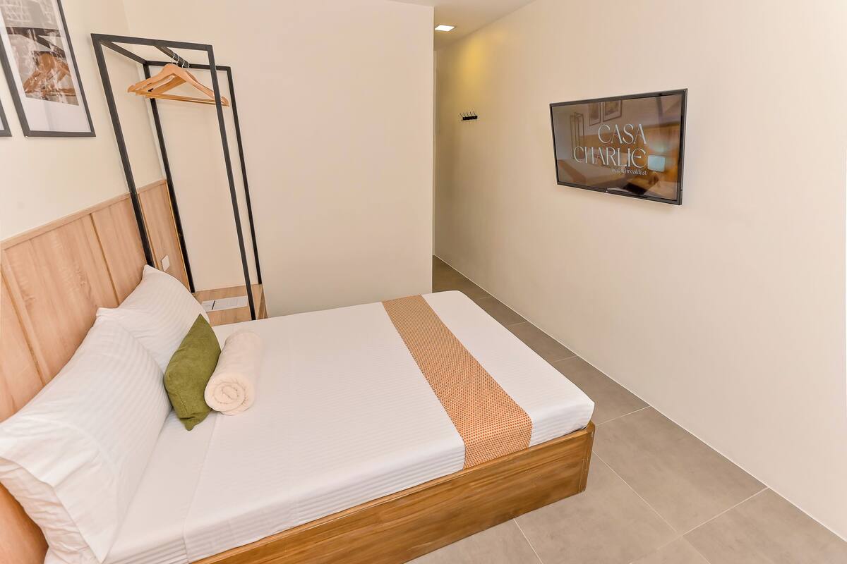 A neatly made bed with a wooden headboard, a green pillow, and a rolled white towel.