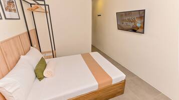 Una cama bien hecha con cabecera de madera, almohada verde y toalla blanca enrollada.