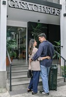 Um casal em frente a um prédio com uma placa que diz 'CASA CHARLIE'.