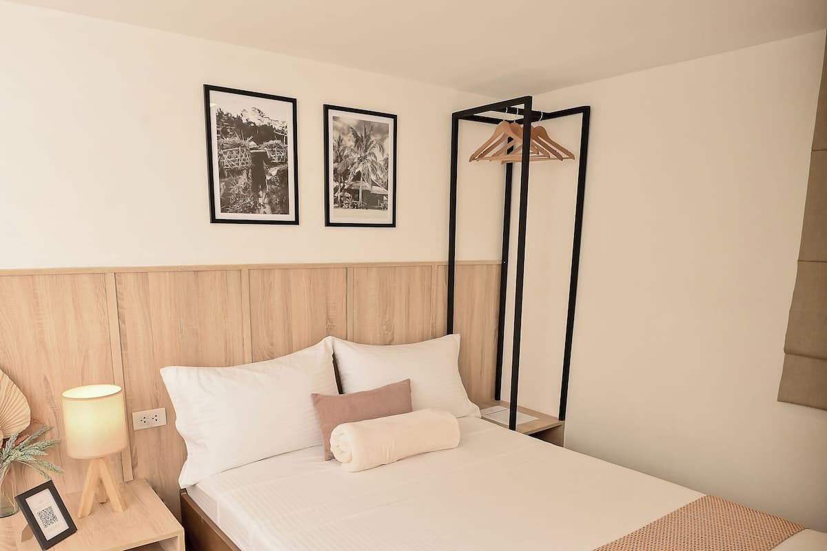 A neatly made bed with a wooden headboard, a bedside table with a lamp, and two framed pictures on the wall.