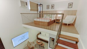 A modern, multi-level apartment with a loft bedroom, a living area with a sofa and chairs, and a staircase.