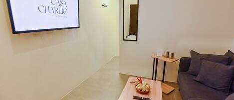 A modern living room with a sofa, a coffee table with a bowl and remote, a TV displaying 'Casa Charlie Bed & Breakfast', and a mirror on the wall.