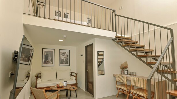 A spacious living area with a sofa, a dining table with chairs, a staircase, and a large mirror.