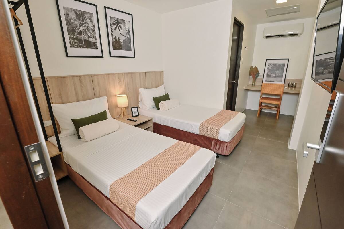 A hotel room with two beds, a desk, a chair, and framed pictures on the wall.