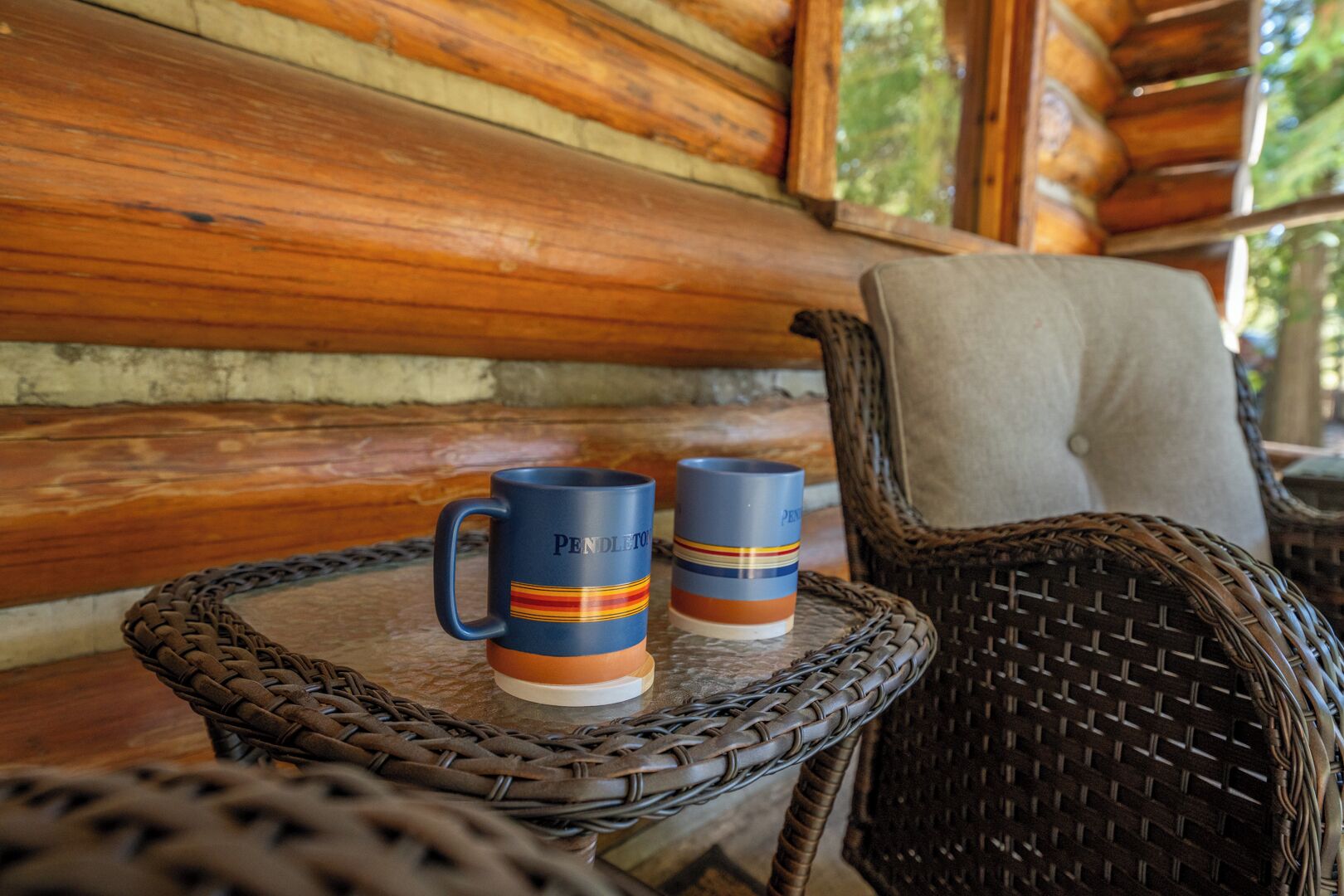Deux tasses sur une table en osier, avec un mur en rondins de bois en arrière-plan.