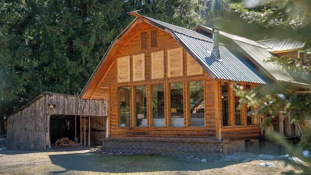 Eine Holzhütte mit großen Fenstern, einem Steinfundament und einem Metalldach.