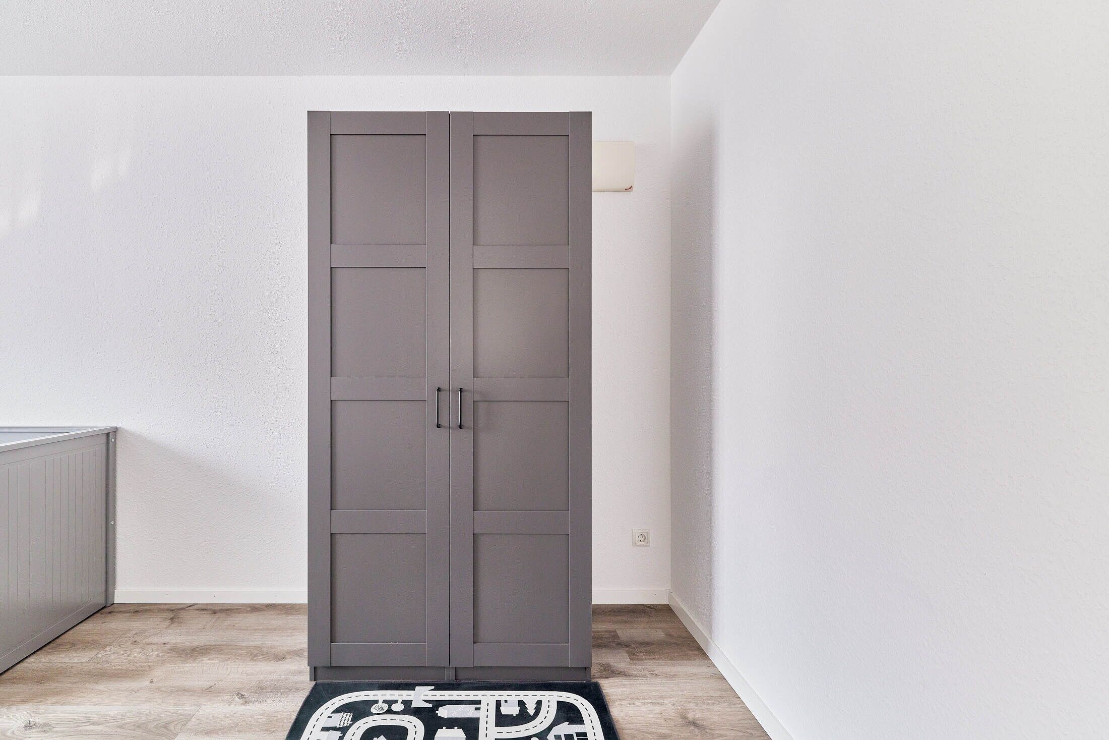 Une armoire grise dans une pièce aux murs blancs et au plancher en bois.