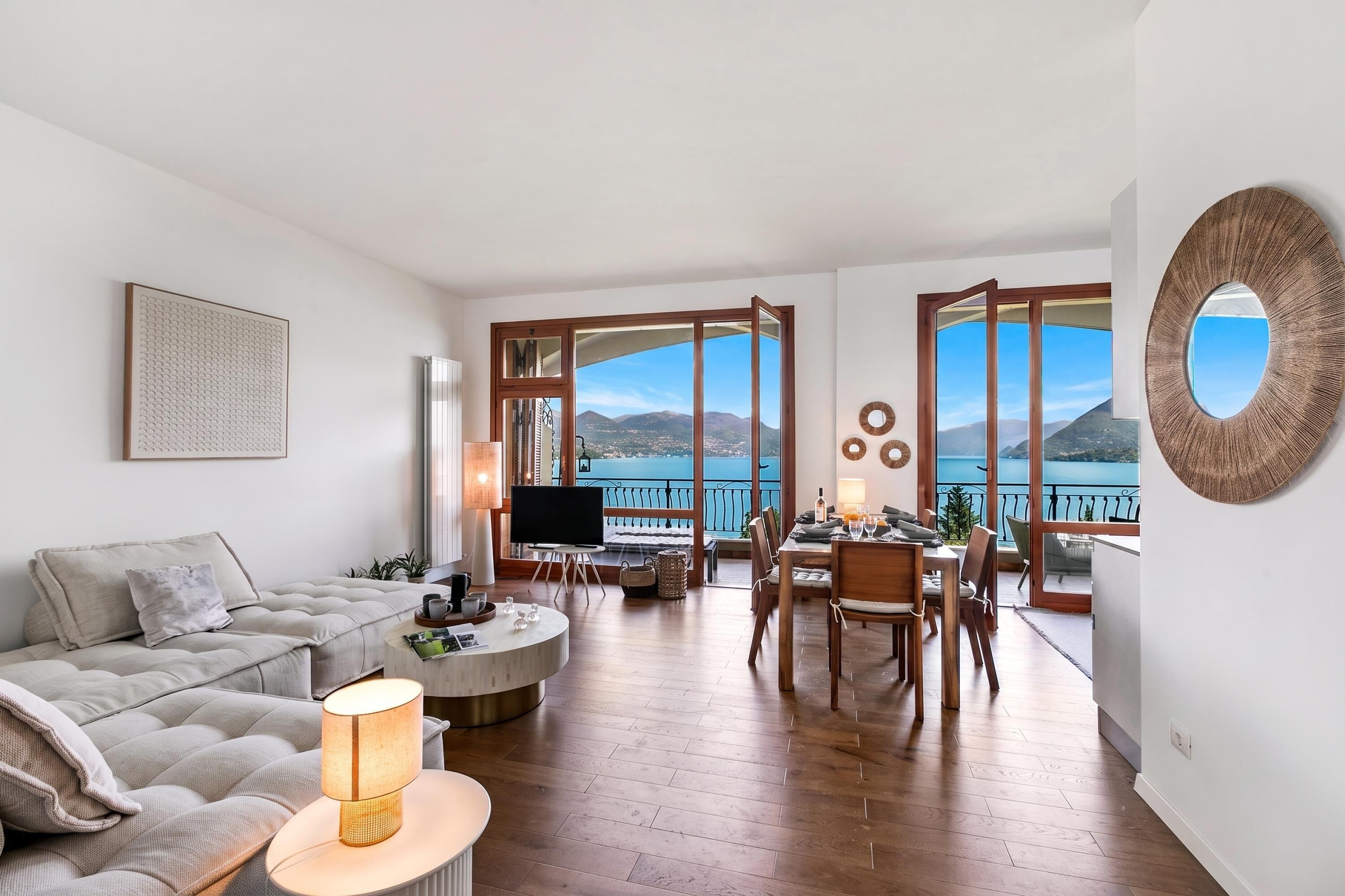 Un salon moderne avec un canapé, une table basse et un téléviseur. Il y a un balcon avec vue sur la mer et les montagnes.