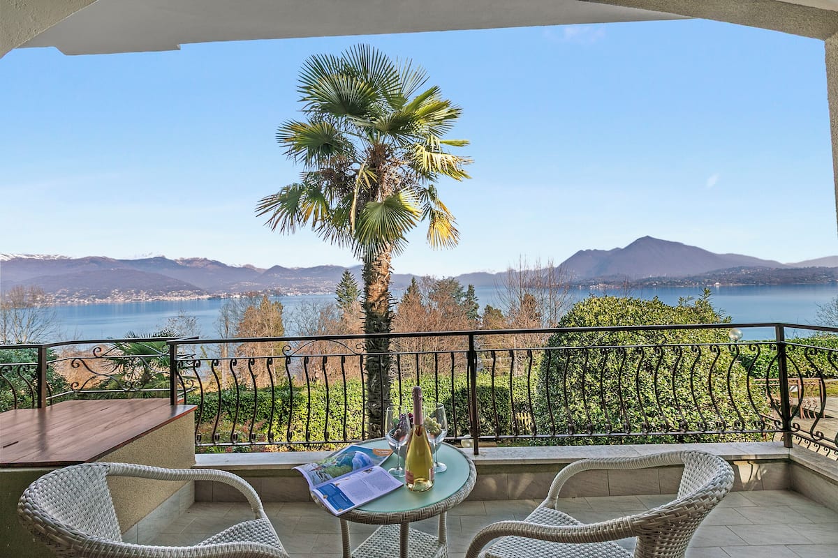 A balcony with wicker chairs, a table, and a bottle of wine.