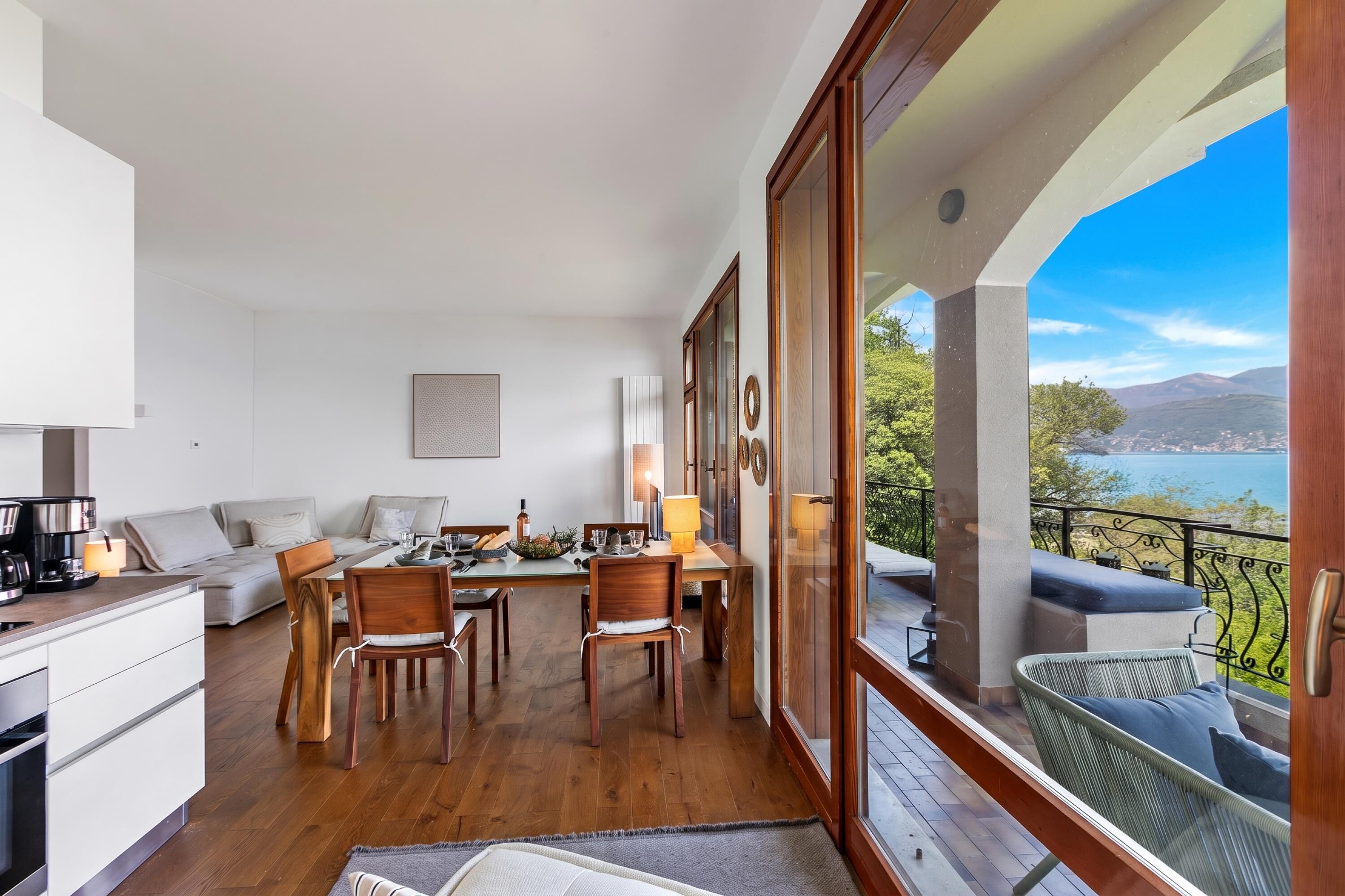 Une cuisine moderne avec des meubles en bois, un coin repas avec une table et des chaises, et un balcon avec vue sur la mer.