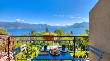 A balcony with a table set for two, overlooking a lake and mountains.