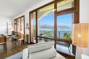 A room with a dining area, a sofa, and large windows with a view of the sea.